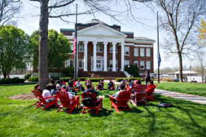 Several students sit in red chairs on the Dell during a class